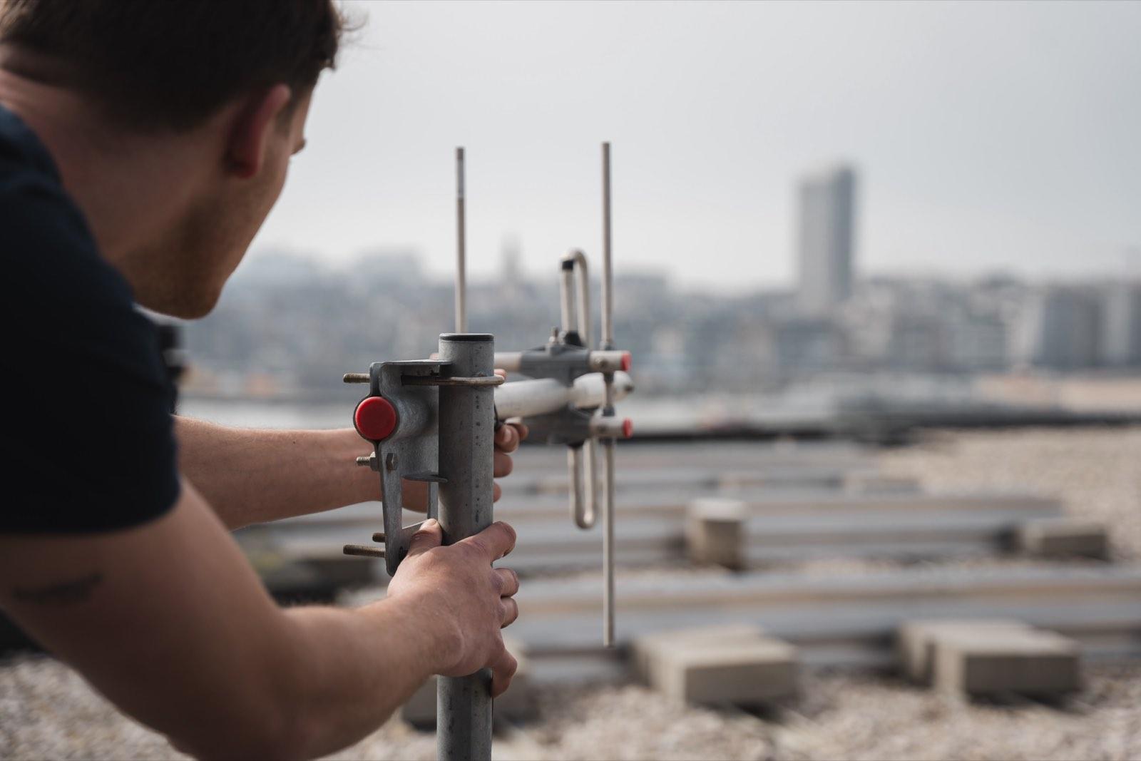 Technicus richt een dakantenne voor ASTRID-binnendekking, met de skyline op de achtergrond.